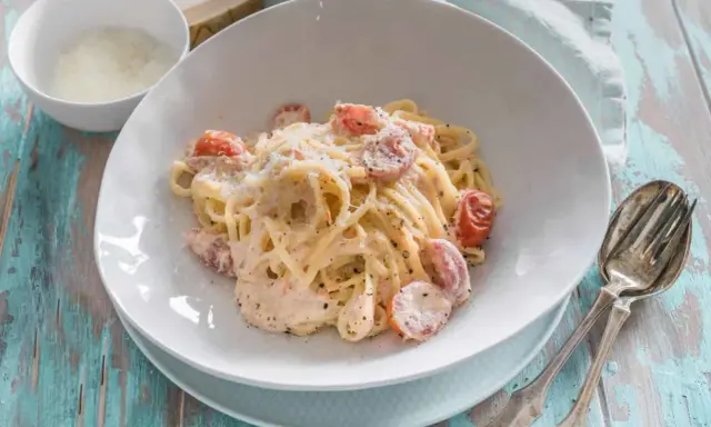 Cremige Pasta al Salmone mit Kirschtomaten und Parmesan, serviert auf einem rustikalen Holztisch.