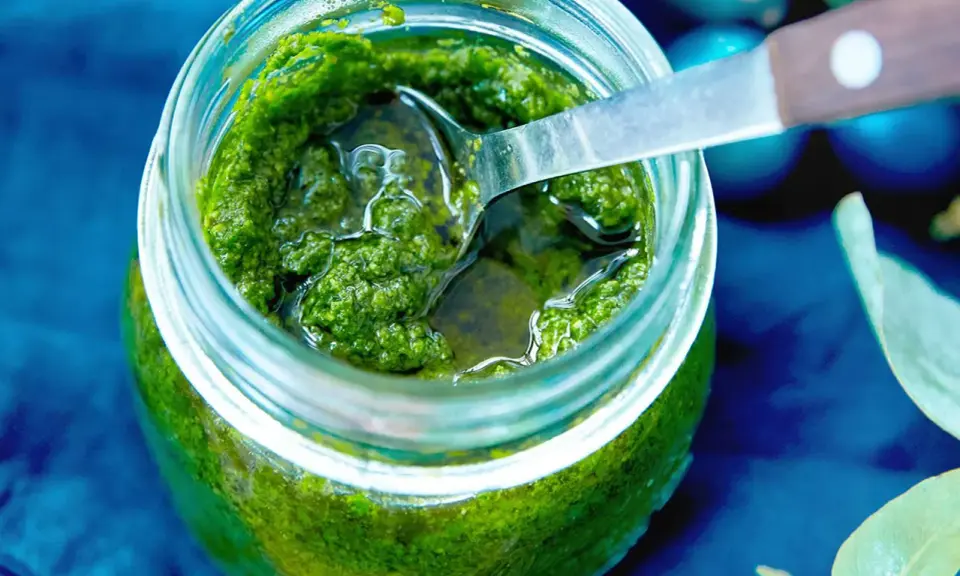 Frisches Rucola Pesto in einem Glas, bereit zum Genießen. Eine Löffelspitze ragt heraus.