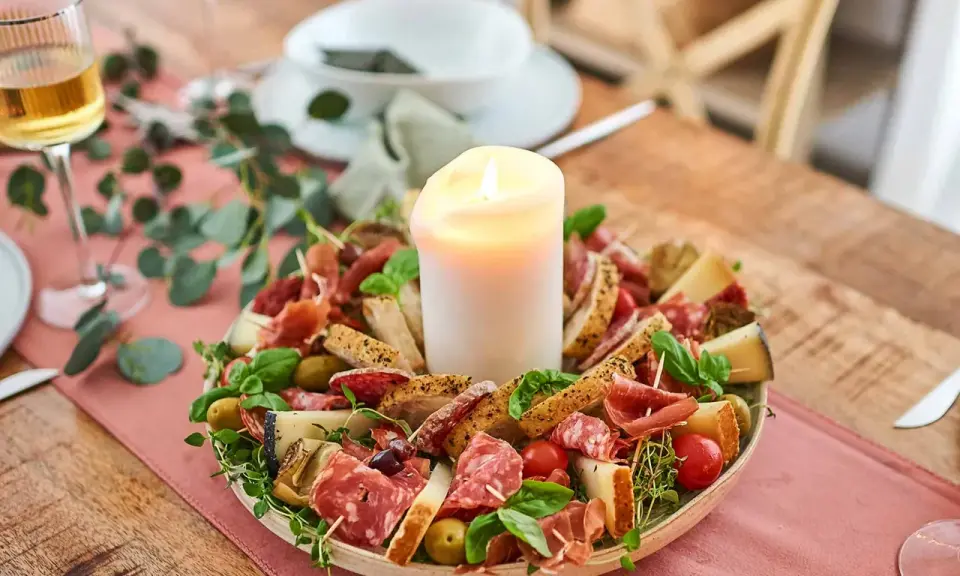 Festliche Platte mit Wurst, Käse, Oliven und Brot, ideal zum Antipasti selber machen. Eine Kerze in der Mitte sorgt für stimmungsvolles Licht.