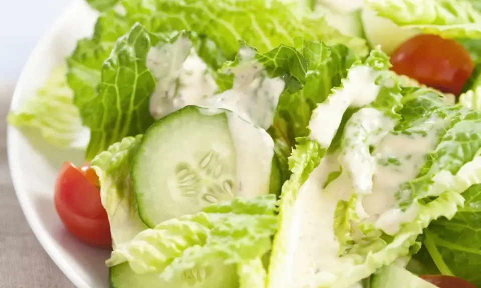 Frischer Romana Salat mit Gurkenscheiben und Tomaten, beträufelt mit cremigem Dressing.