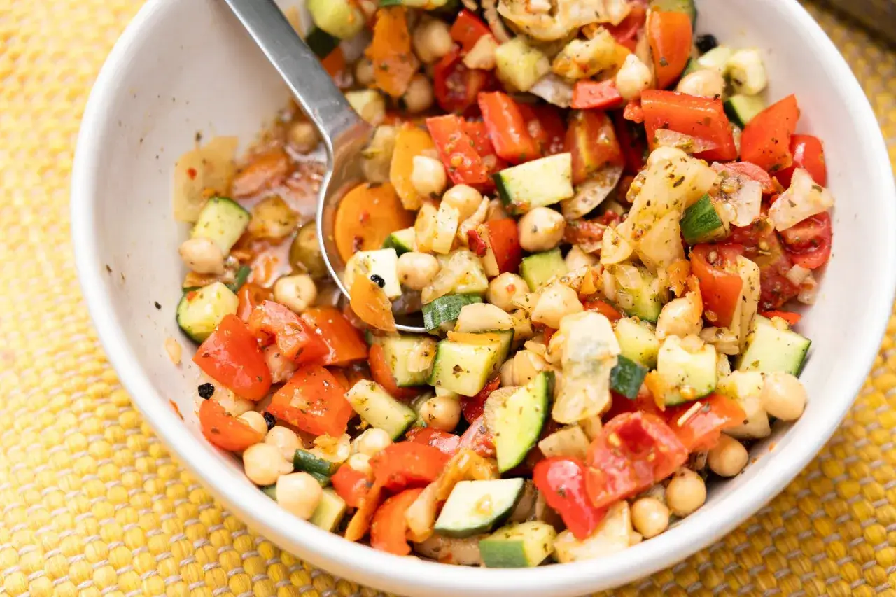 Frischer kichererbsen salat mit Tomaten, Gurken und Karotten, appetitlich in einer weißen Schüssel angerichtet.