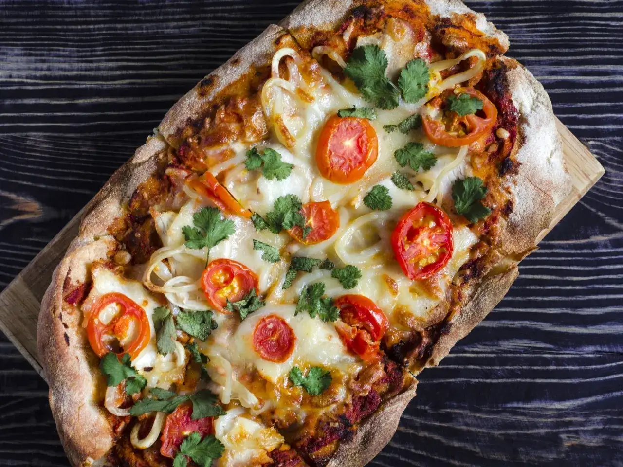 Eine rechteckige Pinsa mit Tomaten, Zwiebeln und K&auml;se, garniert mit Koriander. Die Pinsa herkunft liegt in der r&ouml;mischen Tradition.