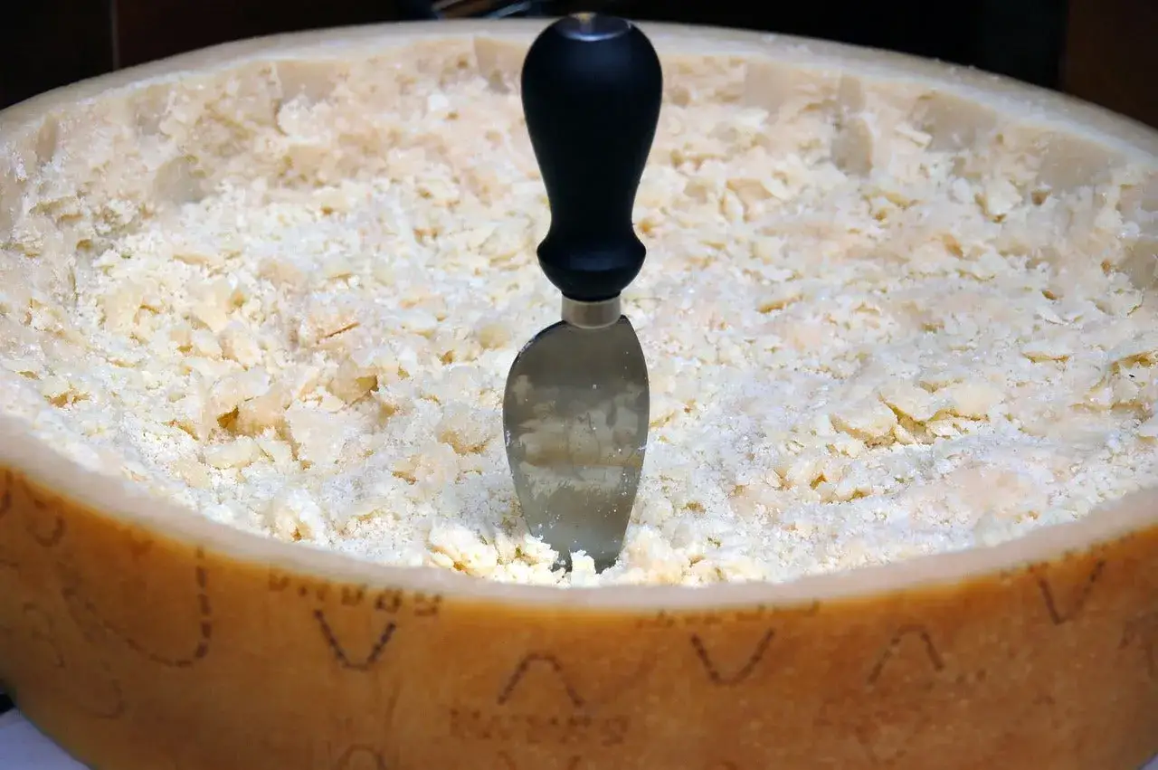 Ein Messer steckt in einem gro&szlig;en Laib Parmesan, der zu feinen Sp&auml;nen zerteilt ist. Ob Pecorino oder Parmesan, dieser K&auml;se ist bereit f&uuml;r Pasta.