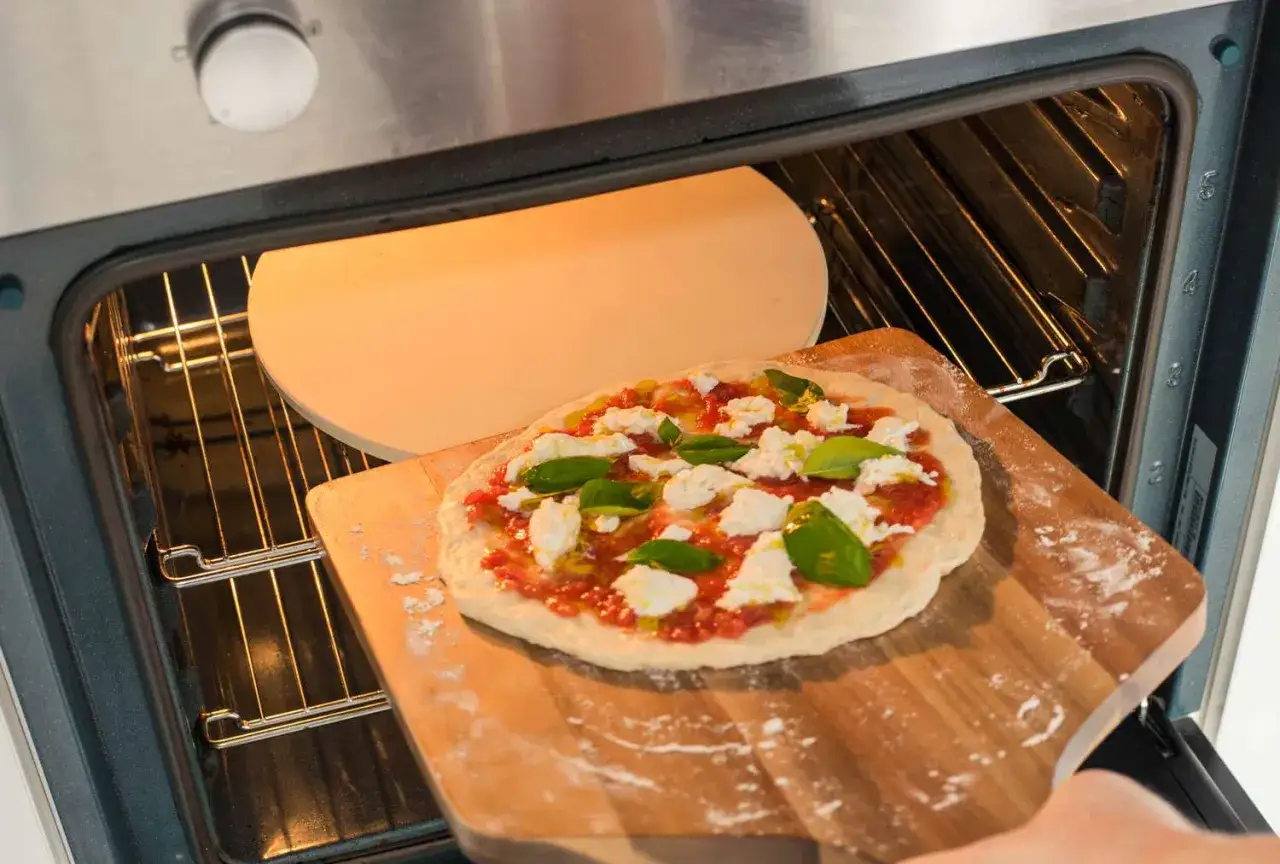 Frisch belegte Pizza mit Mozzarella und Basilikum wird auf einen heißen Pizzastein im Ofen geschoben.