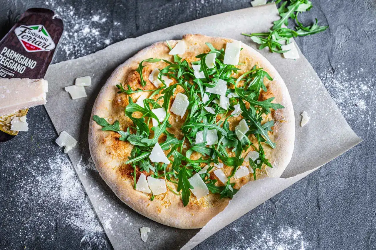 Pizza mit Rucola und Parmesansplittern, statt Tomatensauce eine cremige Basis.