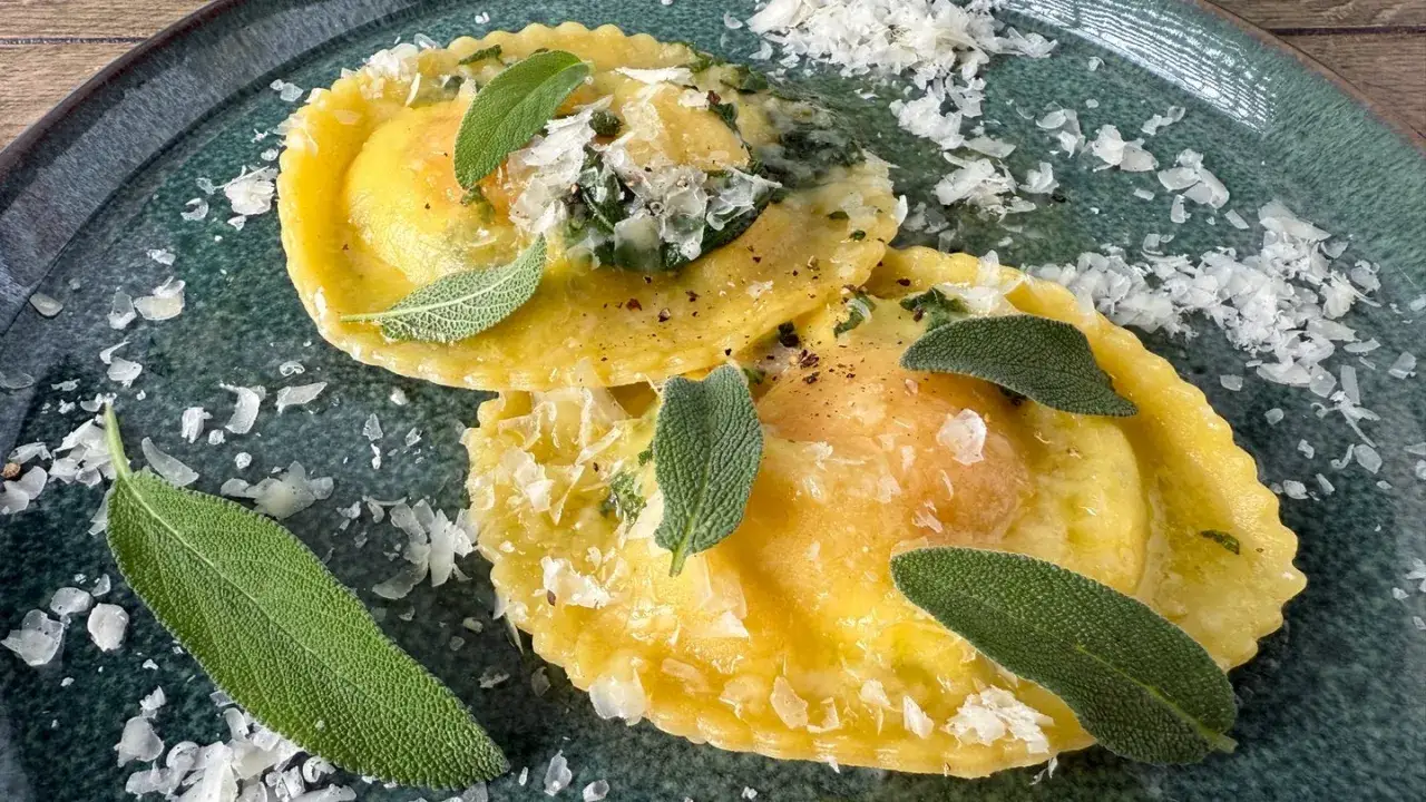 Zwei goldgelbe Mezzelune Spinaci, garniert mit frischem Salbei und Parmesan, auf einem dunkelgr&uuml;nen Teller.