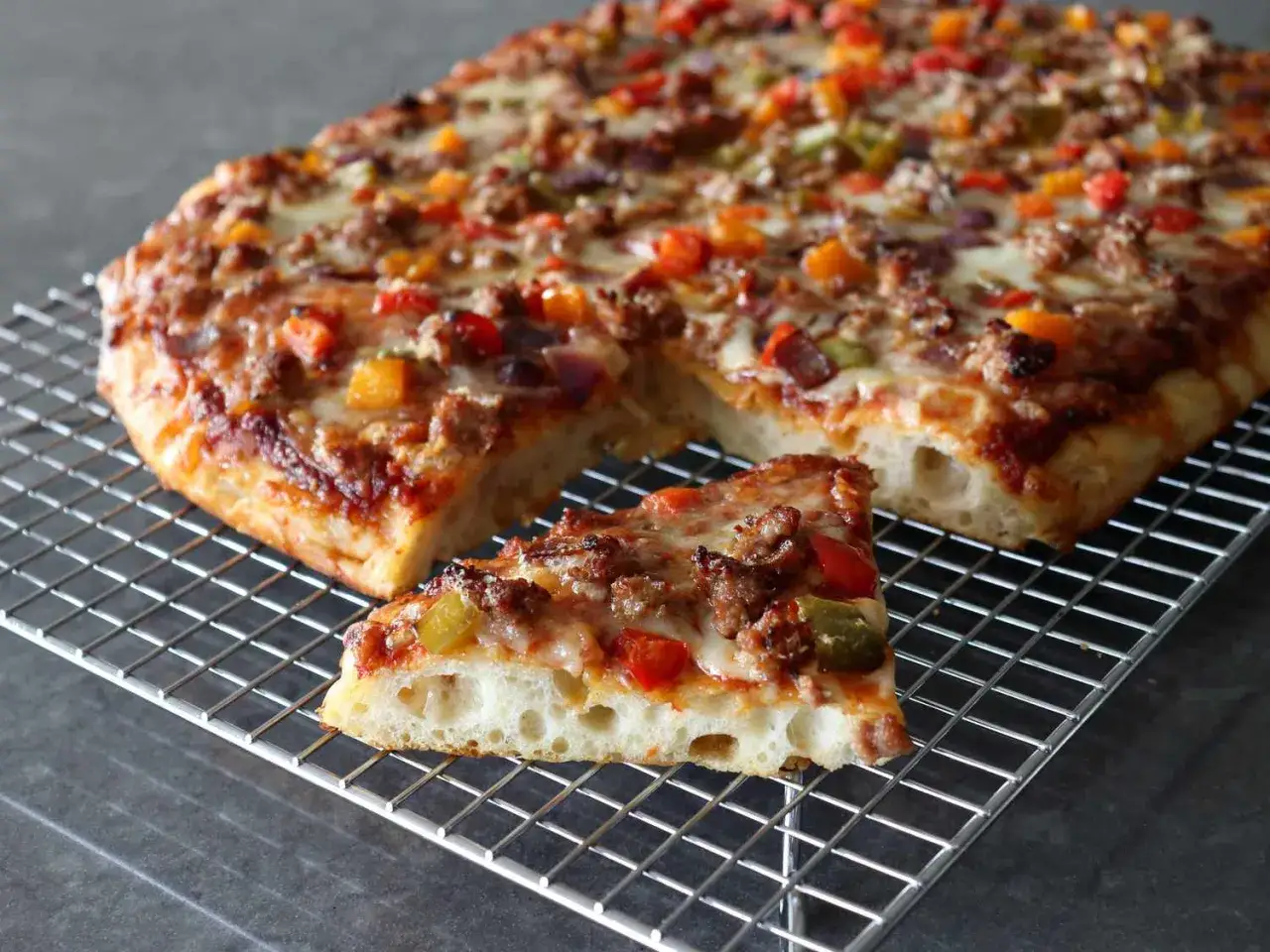 Herzhafte Pizza in Teglia mit Hackfleisch und bunten Paprika auf einem Gitter.