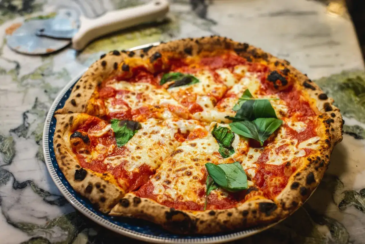 Eine köstliche Pizza Marinara mit geschmolzenem Käse und frischem Basilikum auf einem Marmortisch.