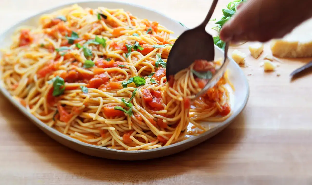 Spaghetti mit einem k&ouml;stlichen Sugo di Pomodoro und frischem Basilikum, bereit zum Servieren. Daneben liegen Parmesan und Kr&auml;uter.