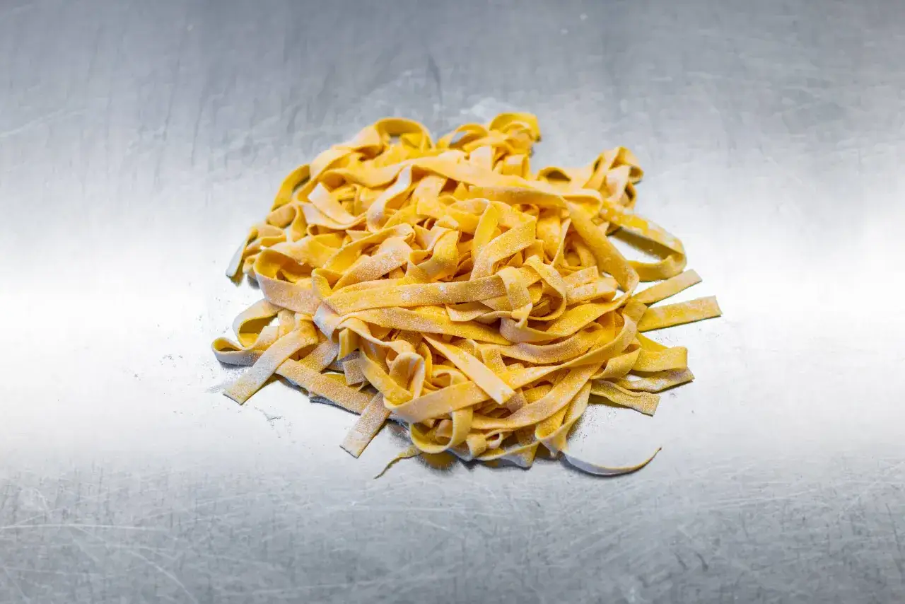 Frische, selbstgemachte Tagliatelle liegen auf einer metallischen Arbeitsfl&auml;che. Ein Beweis daf&uuml;r, dass Tagliatelle selber machen gar nicht so schwer ist.