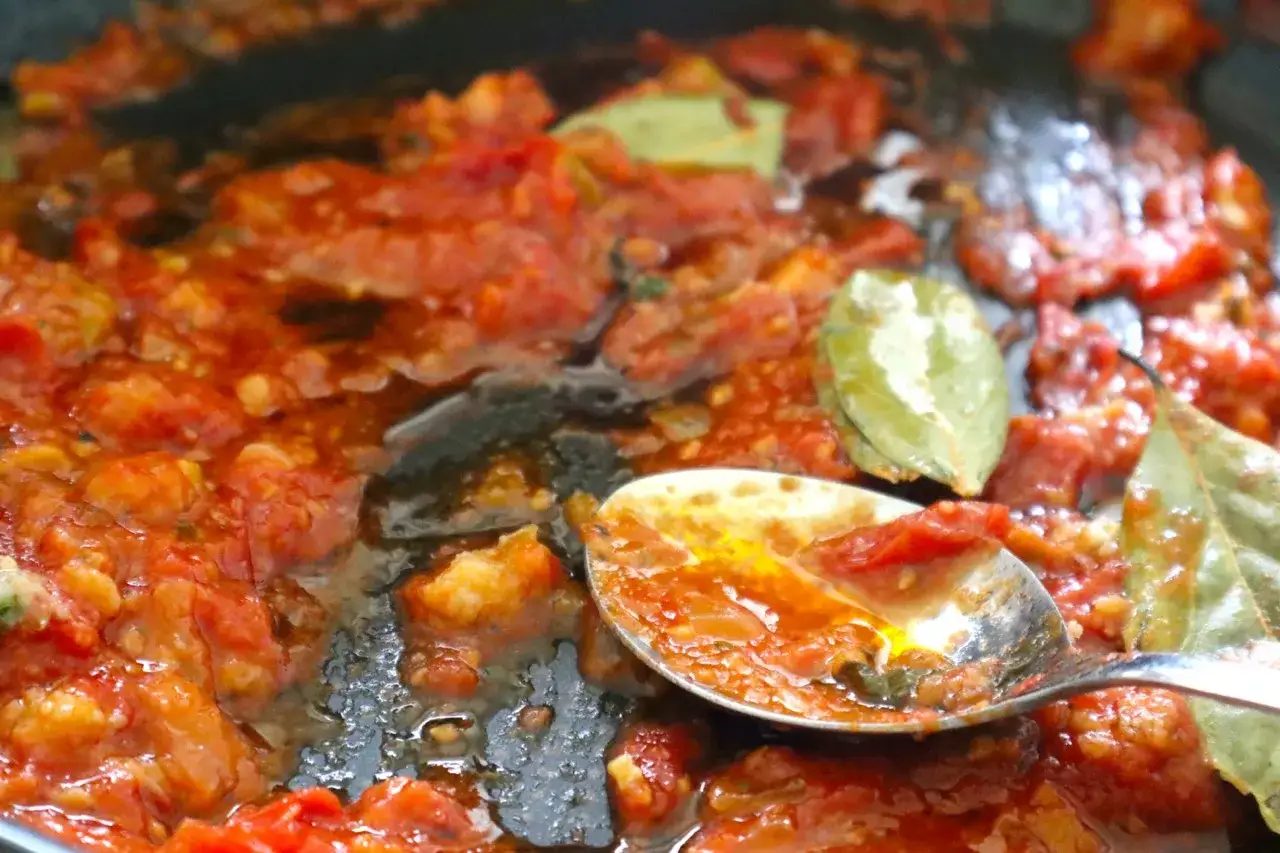 Ein L&ouml;ffel voller k&ouml;stlicher, langsam gekochter San Marzano Tomaten mit Lorbeerbl&auml;ttern in einer Pfanne.