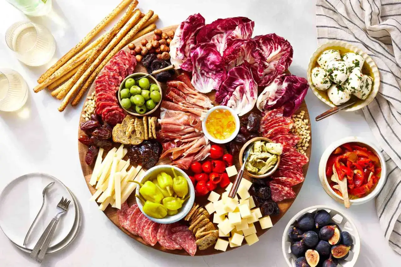 Eine &uuml;ppige italienische Antipasti-Platte dekorieren: Salami, Schinken, K&auml;se, Oliven, Artischocken, Feigen und Grissini.