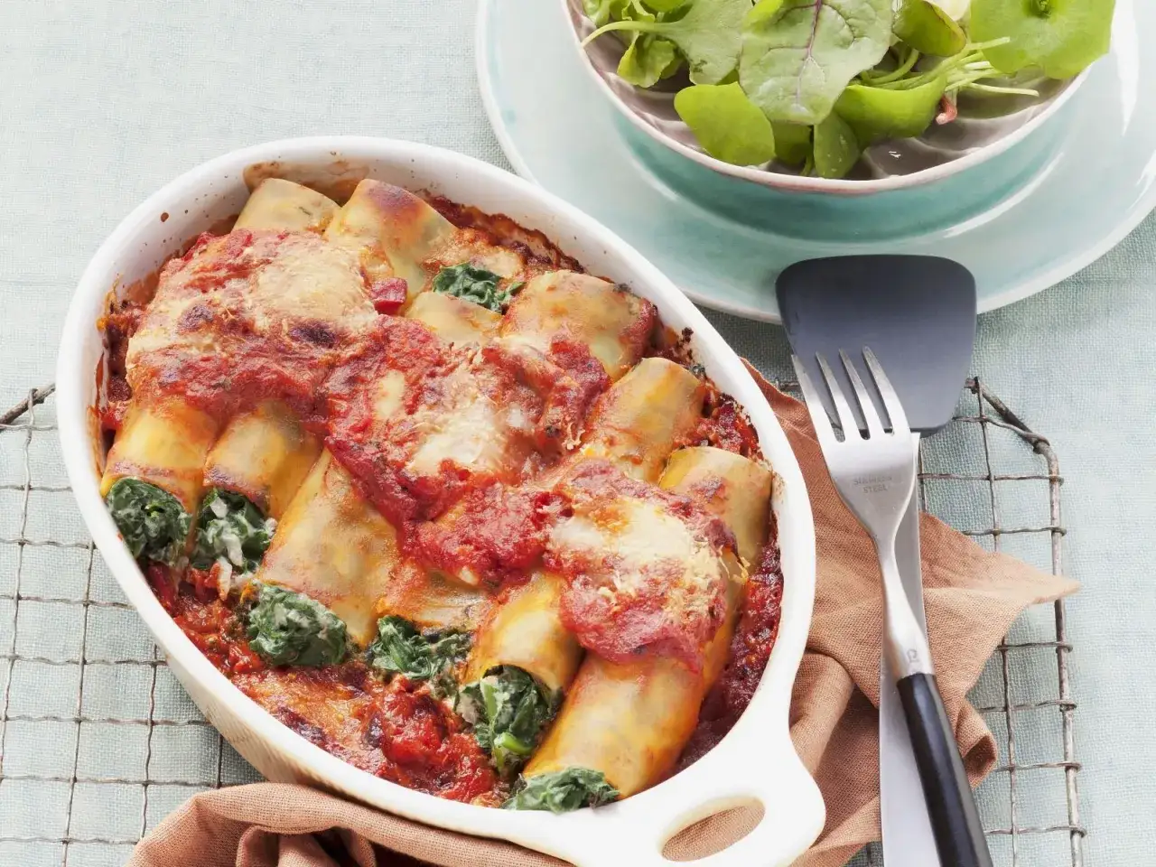 Herzhafte Cannelloni mit Spinat und Tomatensauce, überbacken mit Käse, daneben ein frischer Salat.