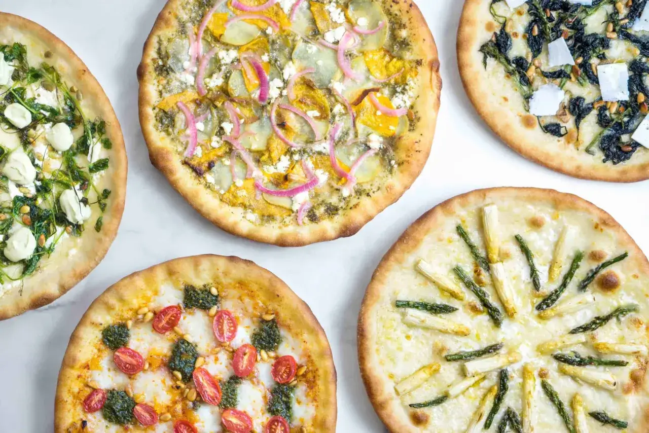 Fünf kreative Pizza-Kombinationen: eine mit Spargel, eine mit Kirschtomaten und Pesto, eine mit Spinat und Pinienkernen, eine mit Kürbis und roten Zwiebeln und eine mit grünem Gemüse und Mozzarella.