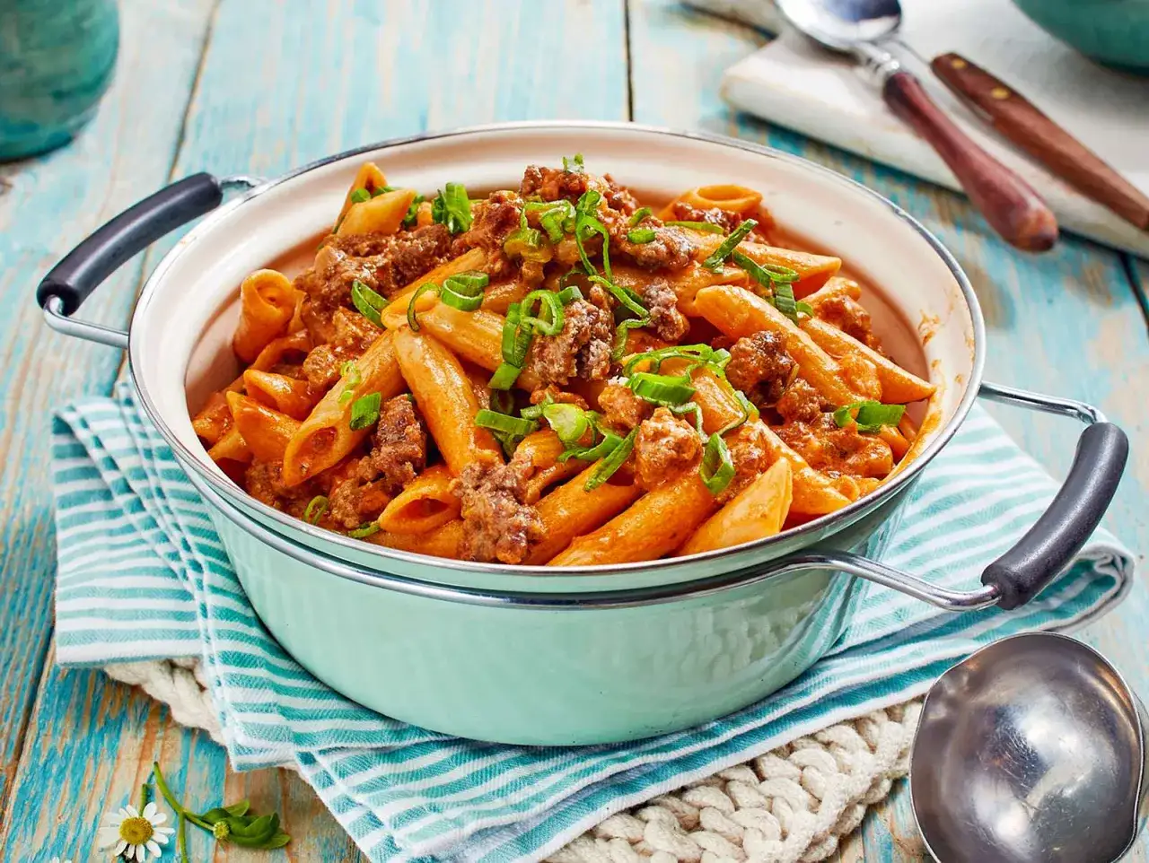 Herzhafte One Pot Pasta mit Hackfleisch und Feta, garniert mit Fr&uuml;hlingszwiebeln, serviert in einer Pastellt&uuml;rkisen Sch&uuml;ssel.