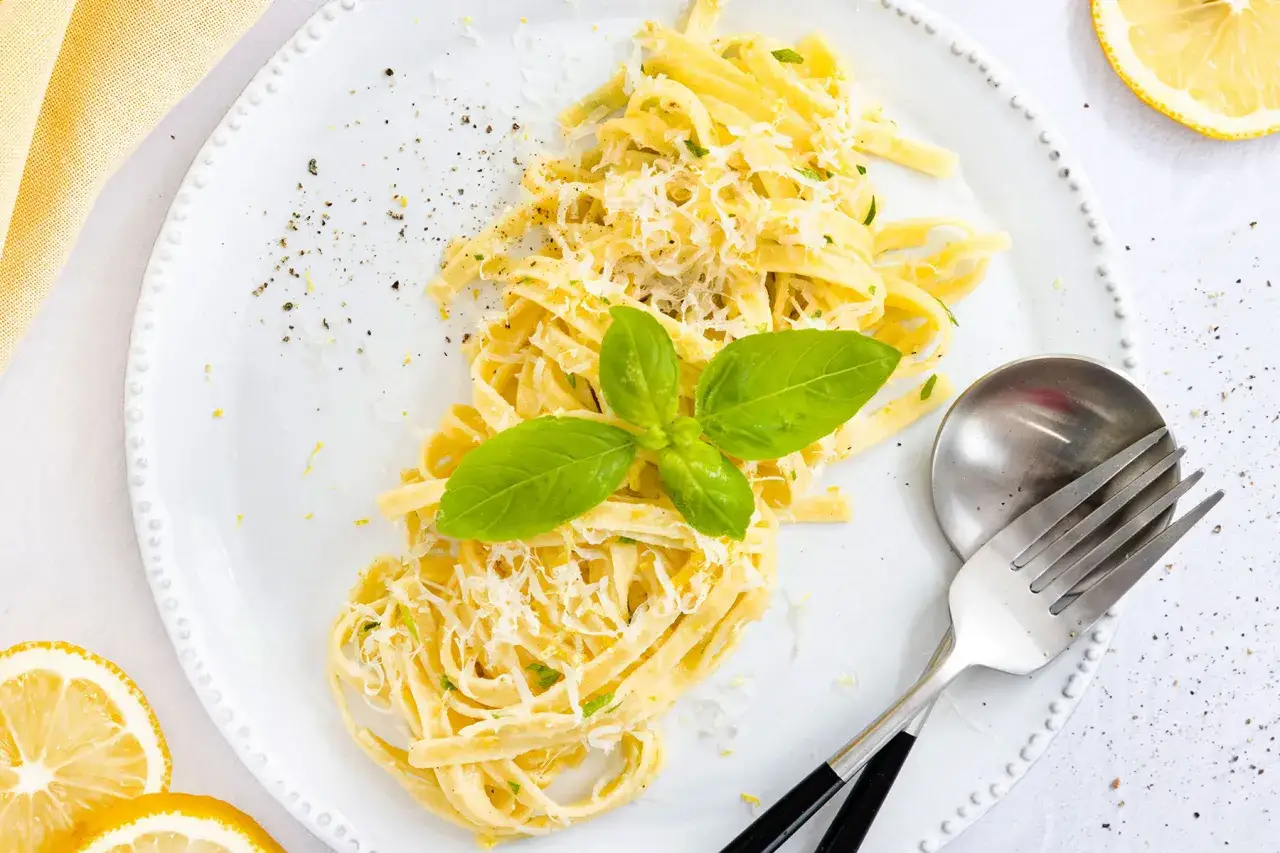 Pasta al limone mit frischem Basilikum und Parmesan, garniert mit Zitronenschale und schwarzem Pfeffer.
