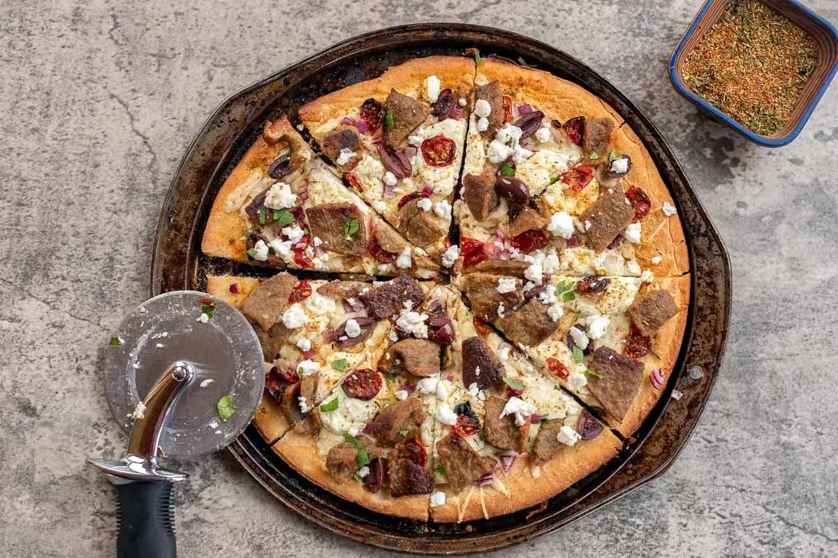 Eine k&ouml;stliche Gyros Pizza mit Fleischst&uuml;cken, Oliven, Feta und roten Zwiebeln, bereit zum Servieren.