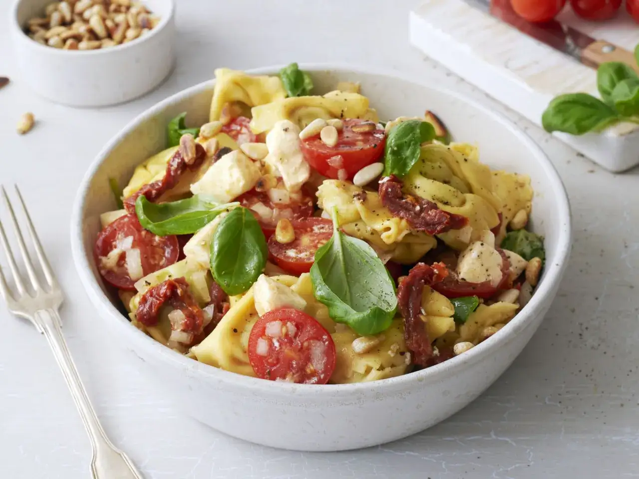 Ein köstlicher Tortellini Salat mit Tomaten, Mozzarella, Basilikum und Pinienkernen in einer Schüssel.