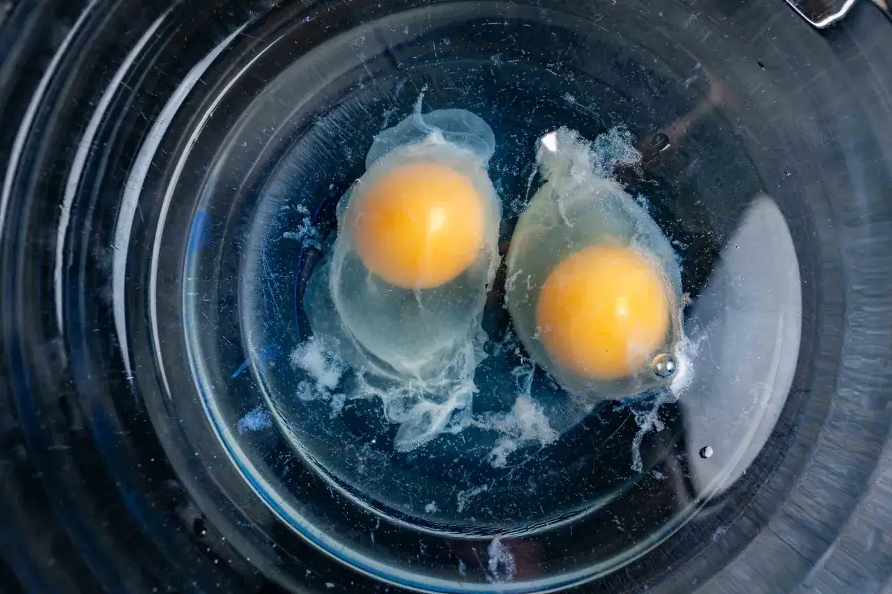 Zwei rohe Eier mit Dottern, die in ihrem Eiwei&szlig; in einer Glassch&uuml;ssel schweben, bereit zum eier pochieren.