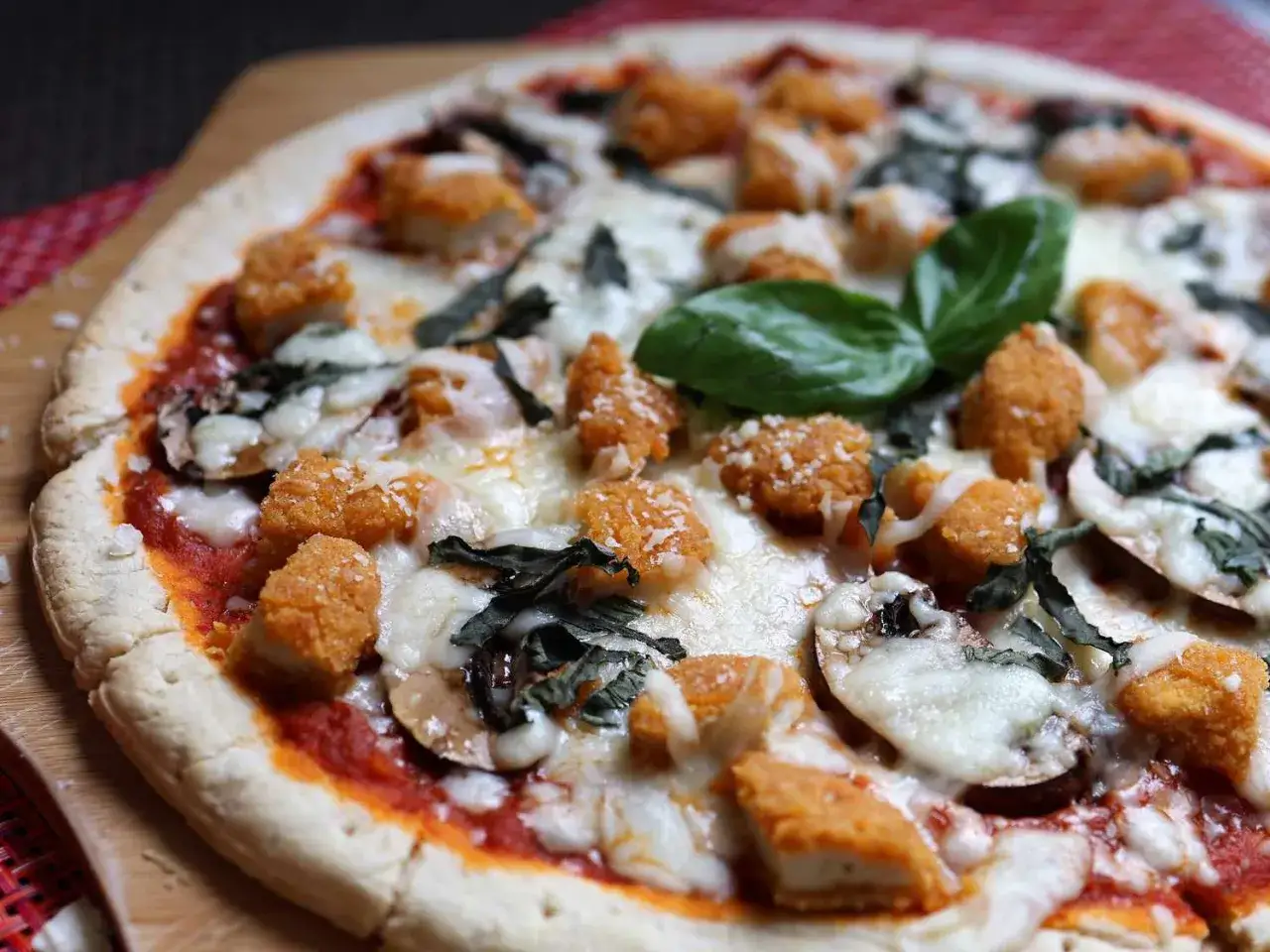 Pizza mit knusprigen H&auml;hnchen-Nuggets, Pilzen, Basilikum und geschmolzenem K&auml;se, bestreut mit feinem parmesan.
