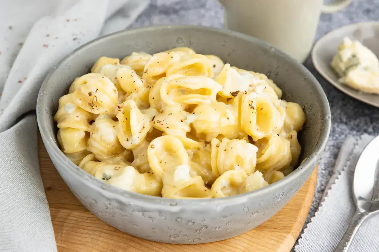 Orecchiette-Nudeln in cremiger Gorgonzola-Sauce, bestreut mit Pfeffer. Ein St&uuml;ck Gorgonzola liegt daneben.