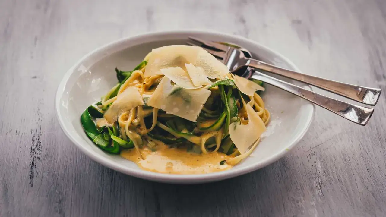 Nudeln mit Spargel und Parmesan in cremiger Sauce, serviert in einer wei&szlig;en Sch&uuml;ssel mit Gabeln.