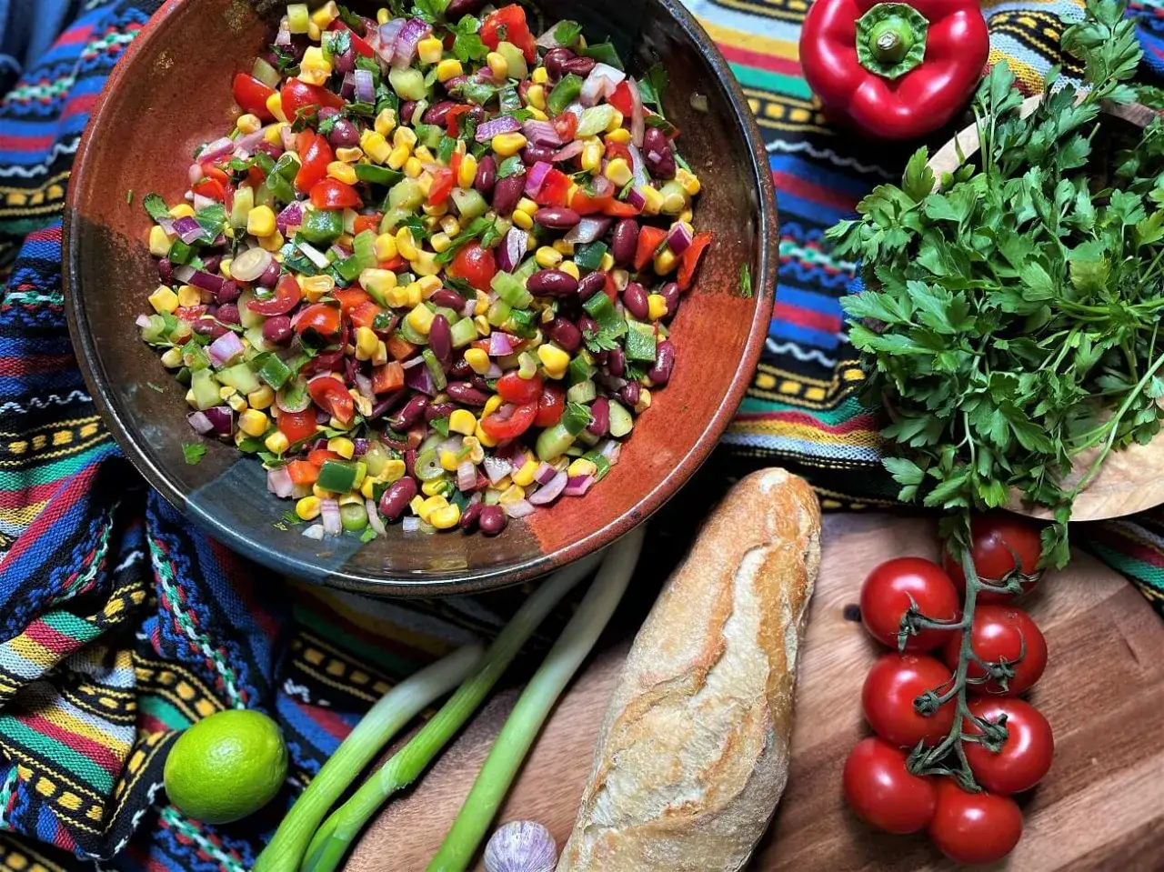 Bunter, frischer Salat mit Mais, Bohnen und Gem&uuml;se, serviert in einer Schale. Daneben liegen ein Baguette, Tomaten und Kr&auml;uter. Ein k&ouml;stlicher italienischer Salat f&uuml;r den Sommer.