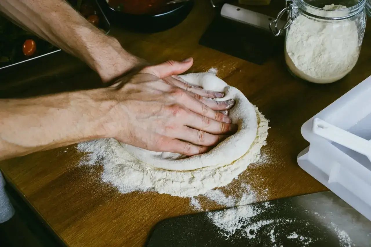 H&auml;nde formen den pizzateig, der sich geschmeidig zusammenzieht. Mehl bedeckt die Holzoberfl&auml;che.