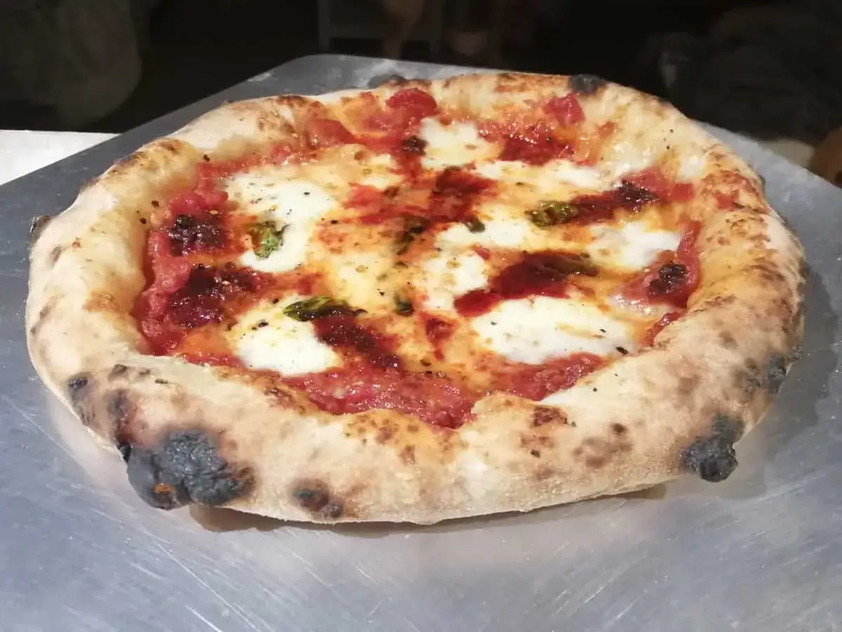Pizza Napoli mit klassischem Belag: Tomatensauce, Mozzarella und Basilikum. Der Rand ist leicht angekohlt.