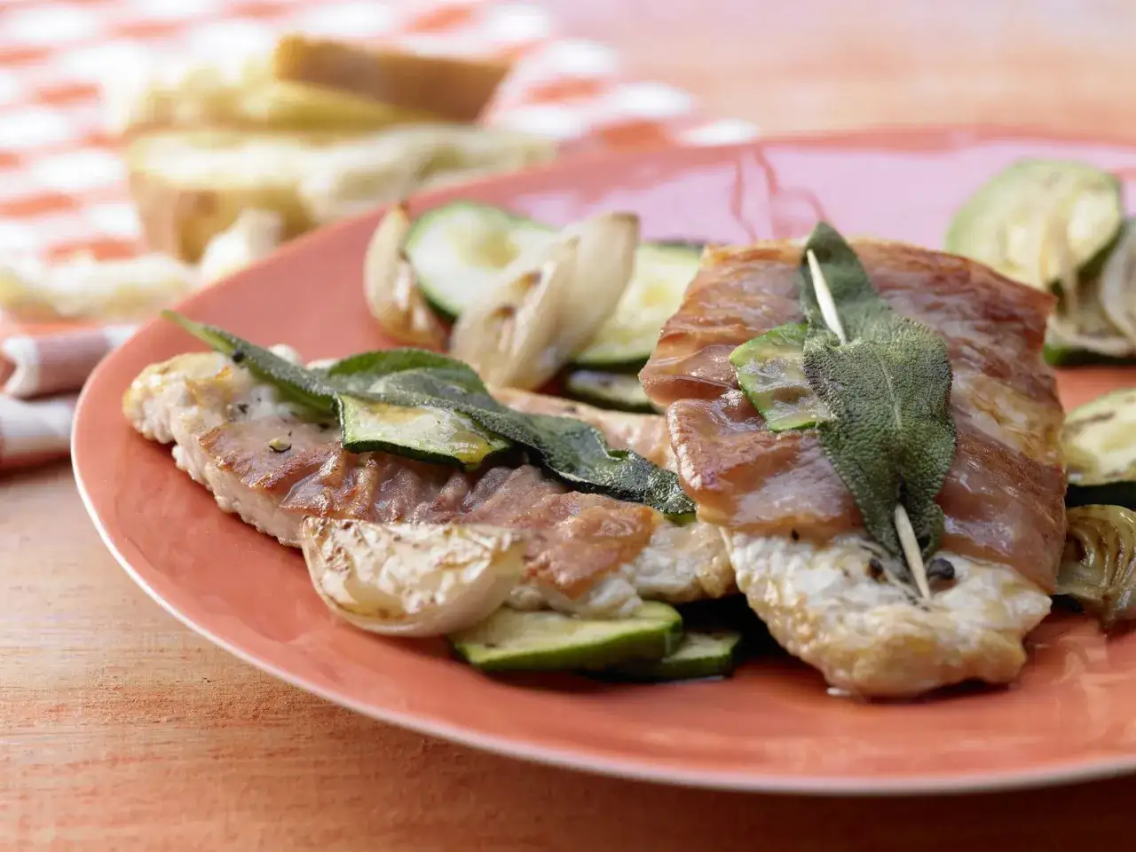 Saltimbocca alla Romana: zarte Kalbsschnitzel mit Salbei und Prosciutto, serviert mit gegrilltem Zucchini und Zwiebeln.