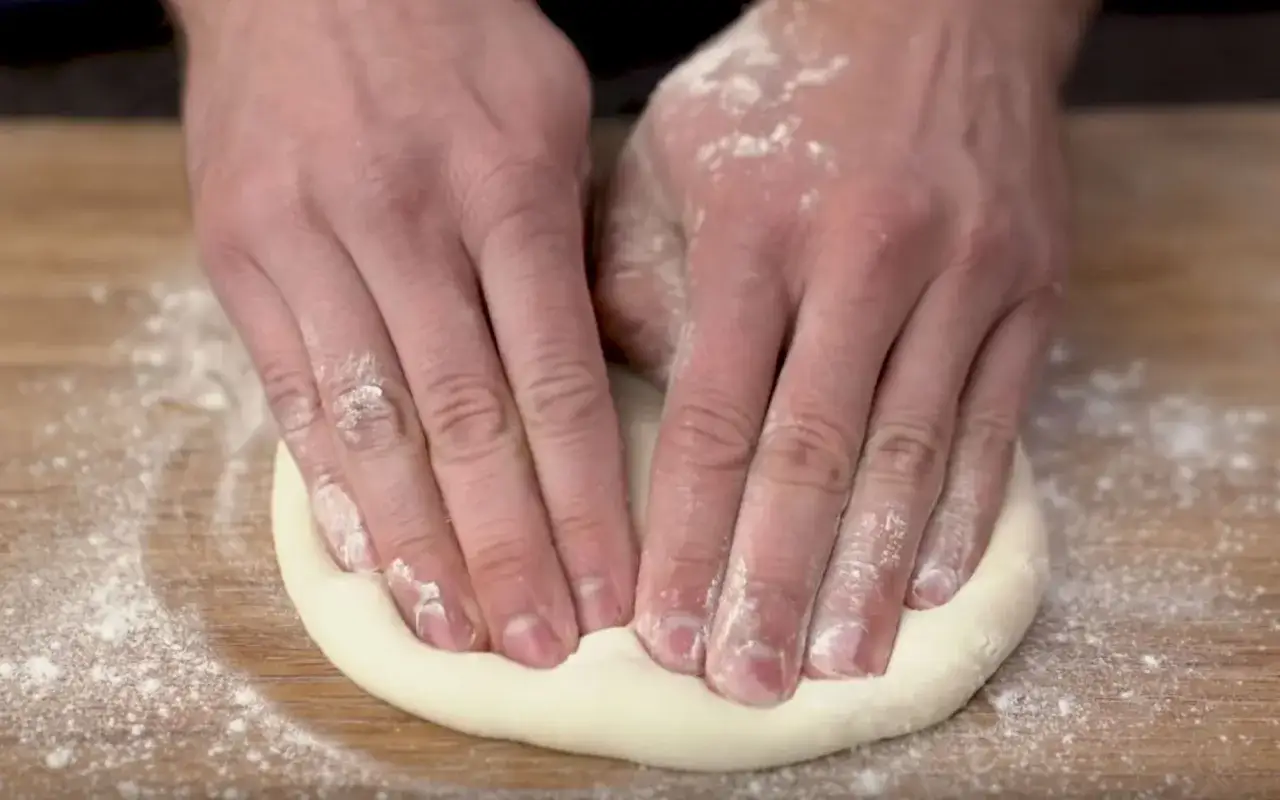 H&auml;nde formen und dehnen den Teig f&uuml;r eine Pizza auf einer bemehlten Holzoberfl&auml;che.