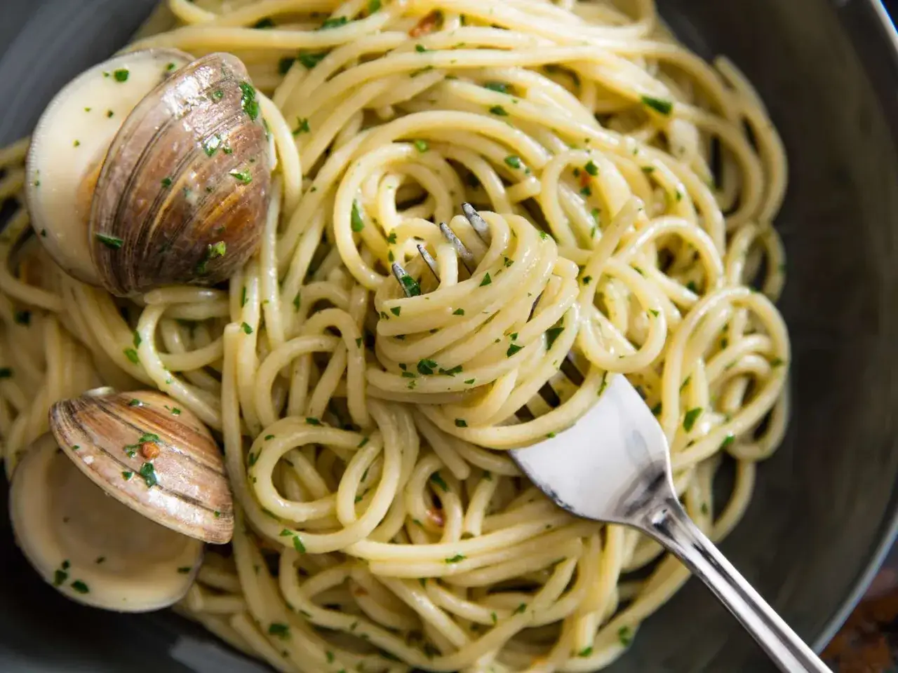 Spaghetti Vongole mit frischen Muscheln und Petersilie, eine Gabel nimmt eine Portion auf.