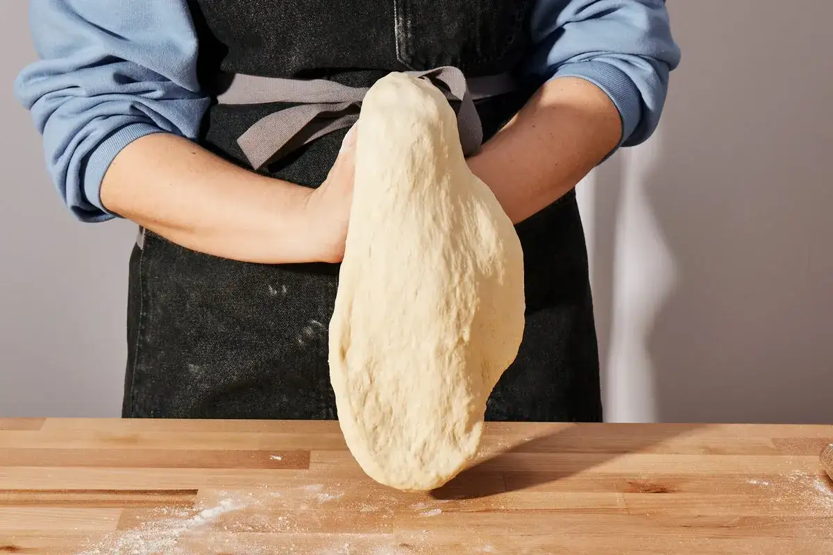 Hände formen einen elastischen Pizzateig. Das Rezept für diesen Teig ist einfach und gelingt jedem.