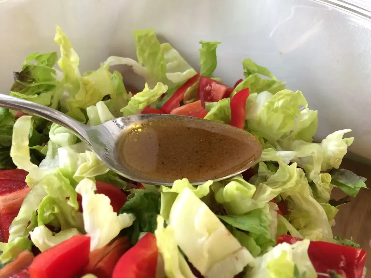 Löffel mit würzigem Balsamico Dressing über frischem Salat mit Tomaten und Paprika.