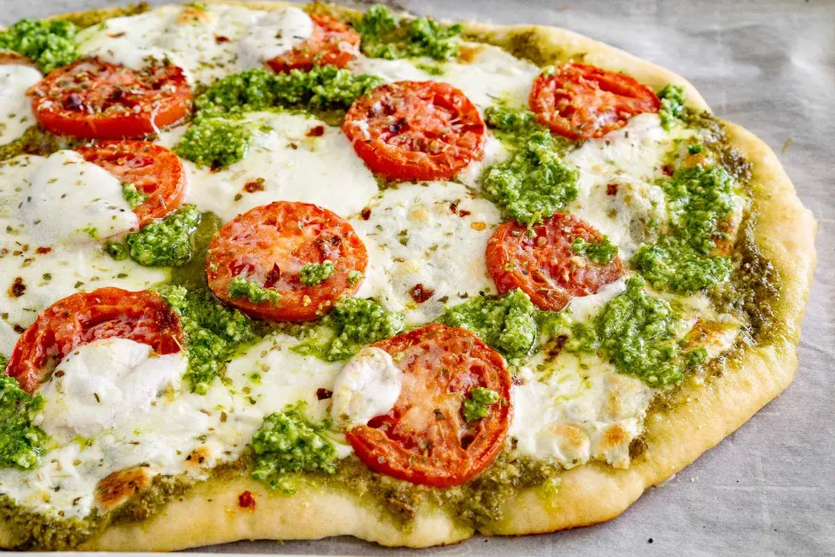 Eine köstliche Pizza mit Pesto, Mozzarella und Tomatenscheiben, die frisch aus dem Ofen kommt.