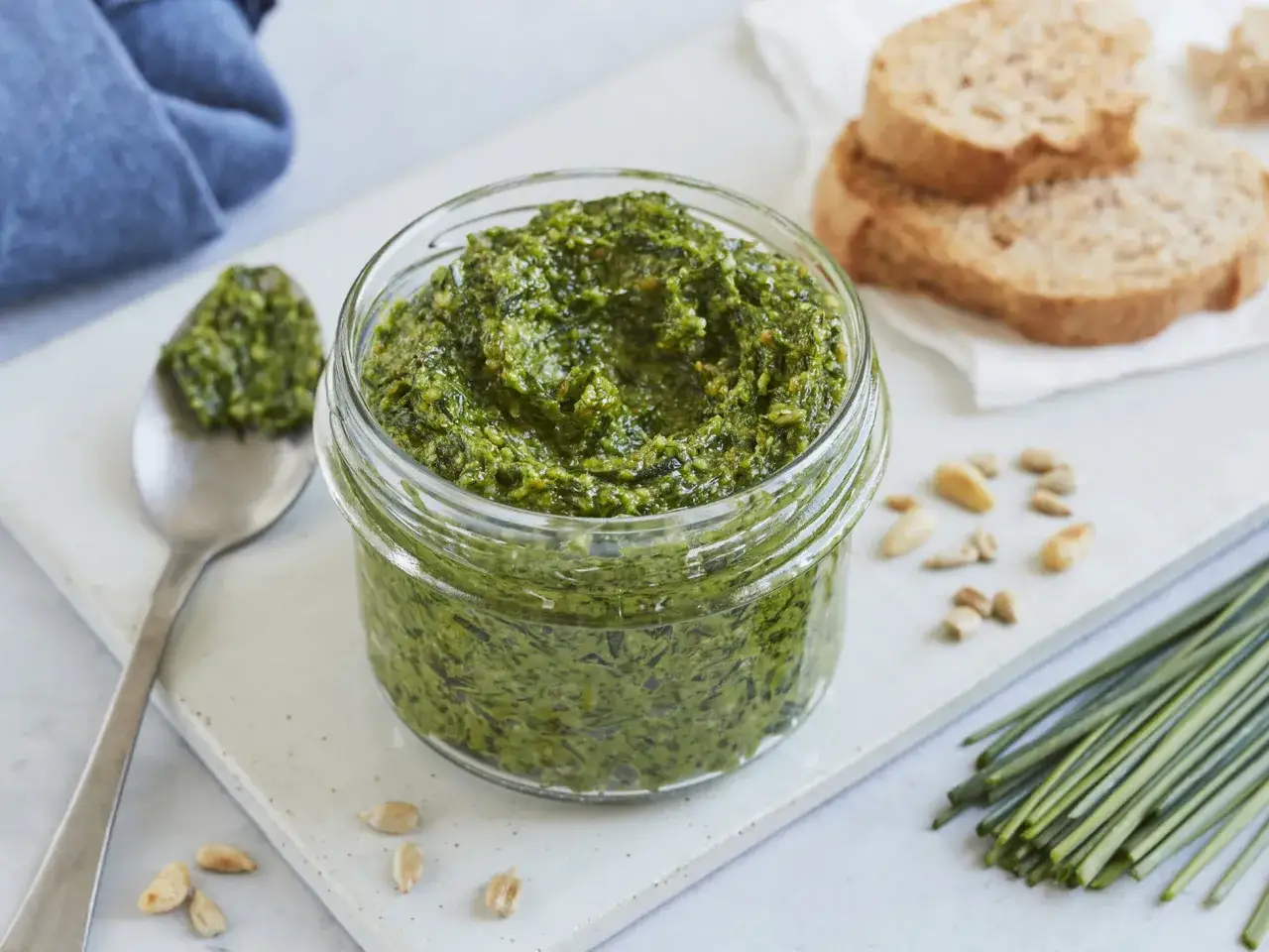 Frisches schnittlauch pesto in einem Glas, daneben eine L&ouml;ffelportion, Brot und Pinienkerne.