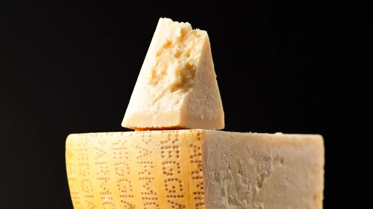 Ein St&uuml;ck Parmigiano Reggiano, der ber&uuml;hmte Parmesan, liegt auf einem gr&ouml;&szlig;eren St&uuml;ck desselben K&auml;ses.