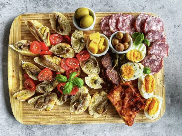 Ein köstlicher Antipasti-Abend mit Bruschetta, Sardellen, Tomaten, Oliven, Käse, Eiern und Salami auf einem Holzbrett.