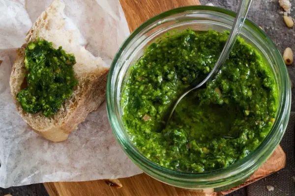 Frisches schnittlauch pesto in einem Glas, mit einem Löffel darin. Ein Stück Brot mit dem grünen Pesto darauf liegt daneben.
