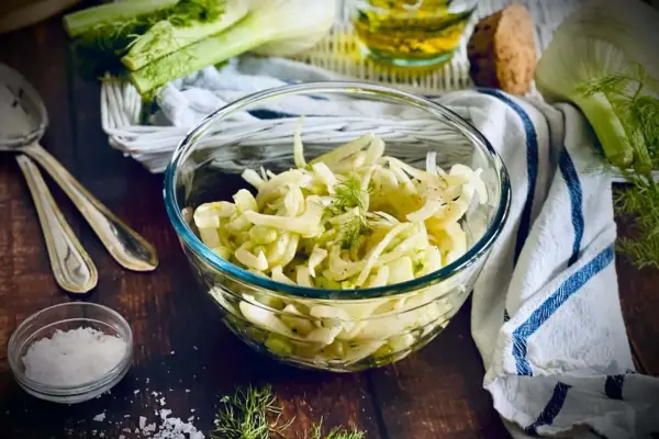 Frischer Fenchel Salat in einer Glasschüssel, garniert mit Dill. Daneben liegen Löffel und eine kleine Schale mit Salz.