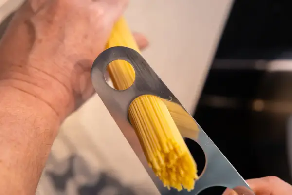 Ein Mann misst mit einem Metallwerkzeug die richtige Menge Spaghetti pro Person ab.