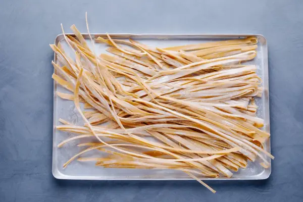 Frische, selbstgemachte Tagliatelle liegen auf einem Blech, bereit zum Kochen. Das Ergebnis von Tagliatelle selber machen.