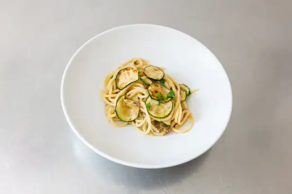 Spaghetti alla Nerano, ein cremiges Pastagericht mit gebratenen Zucchinischeiben, garniert mit frischen Kräutern, serviert auf einem weißen Teller.