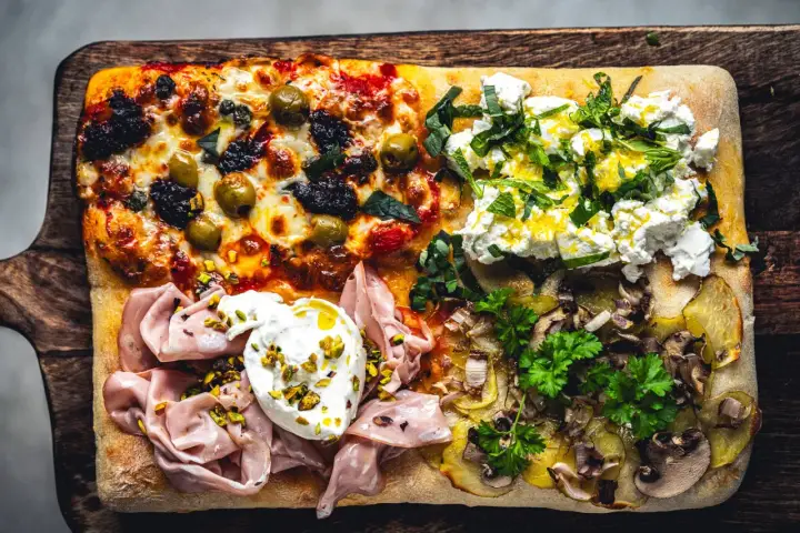 Vier verschiedene Beläge auf einer rechteckigen Pizza in Teglia: Oliven & Tomaten, Ricotta & Kräuter, Mortadella & Burrata, Kartoffeln & Pilze.