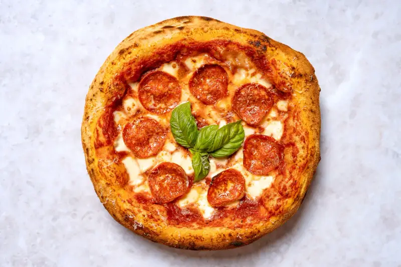 Eine köstliche New York Style Pizza mit Salami und frischem Basilikum, bereit zum Genießen.