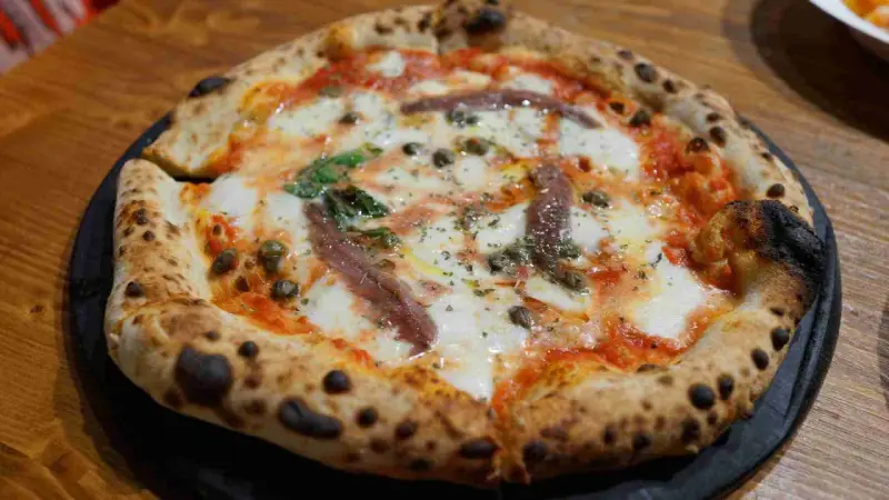 Eine original Pizza mit geschmolzenem Käse, Sardellen, Kapern und Basilikum.