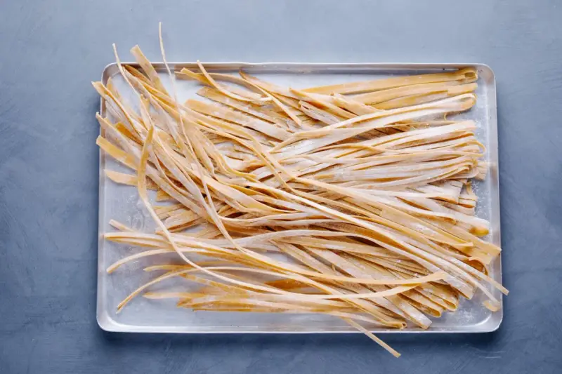 Frische, selbstgemachte Tagliatelle liegen auf einem Blech, bereit zum Kochen. Das Ergebnis von Tagliatelle selber machen.