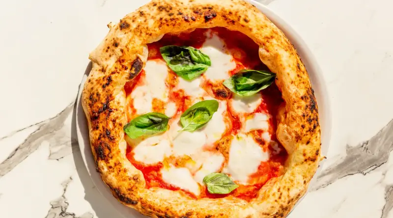 Eine klassische Pizza Napoli mit Tomaten, Mozzarella und frischem Basilikum. Der Belag ist einfach, aber perfekt für diese neapolitanische Spezialität.