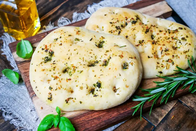 Zwei fluffige Pizzabrote mit Kräutern, perfekt gebacken mit Trockenhefe. Daneben frisches Basilikum und Rosmarin.
