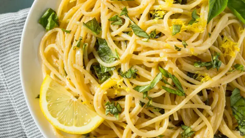 Spaghetti al limone, garniert mit frischem Basilikum und Zitronenschale, serviert mit einer Zitronenspalte.